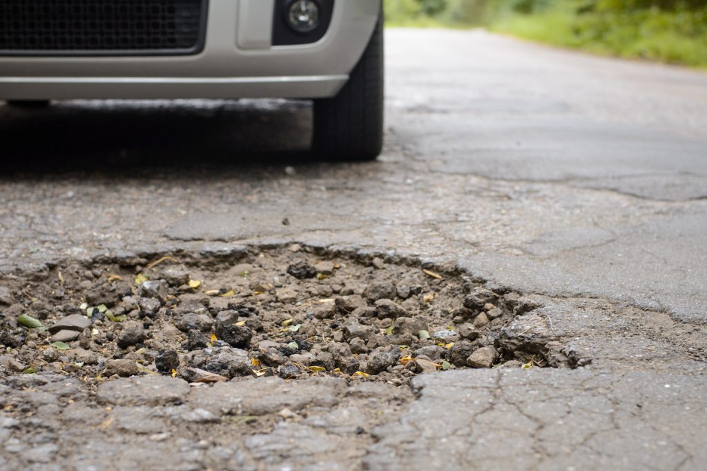 Damaged road full of cracked potholes in pavement