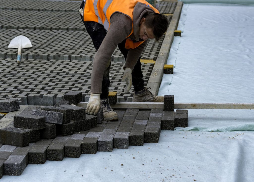Construction worker laying interlocking paving concrete onto sheet nonwoven bedding sand and fitting them into place
