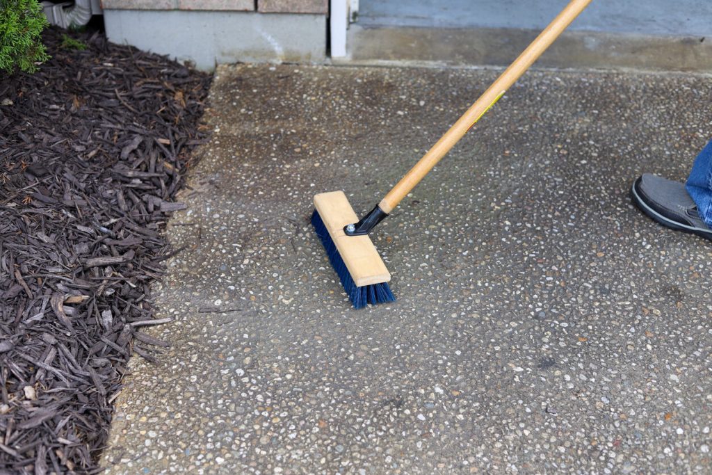 Asphalt driveway maintenance. A man cleaning a driveway with a broom