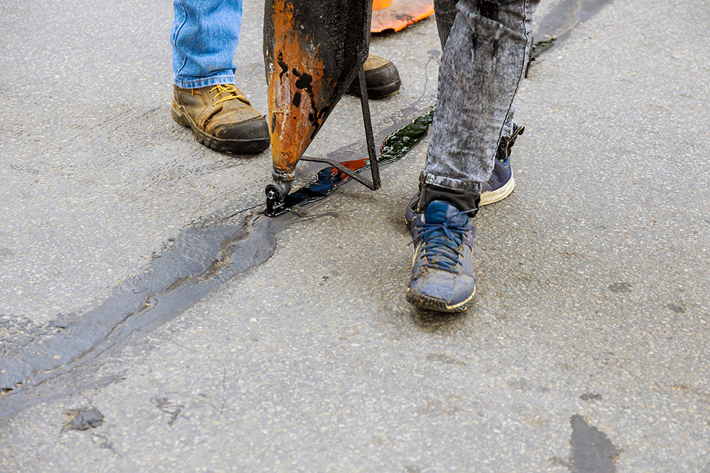 Road surface restoration work in the worker performs on road patcher work on the repair by crack sealing