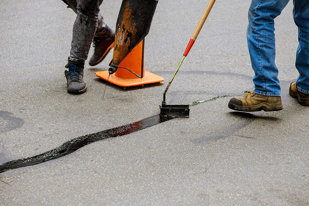 Road surface restoration work in the worker performs on road patcher work on the repair by crack sealing with coated by bitumen emulsion asphalt surface