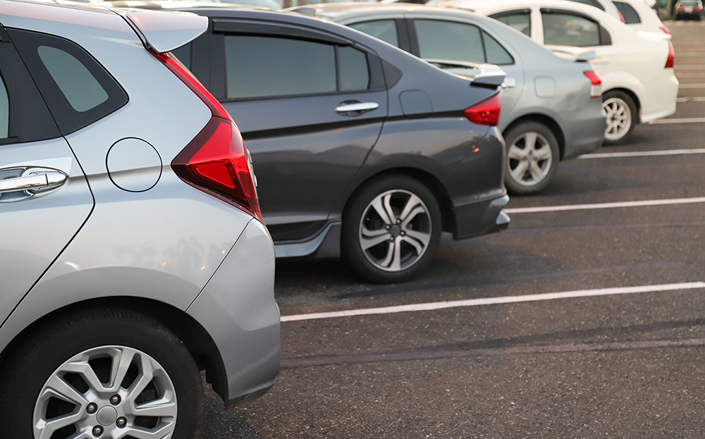 Closeup of back or rear side of cars parking in outdoor parking area in twilight evening with asphalt paving issues