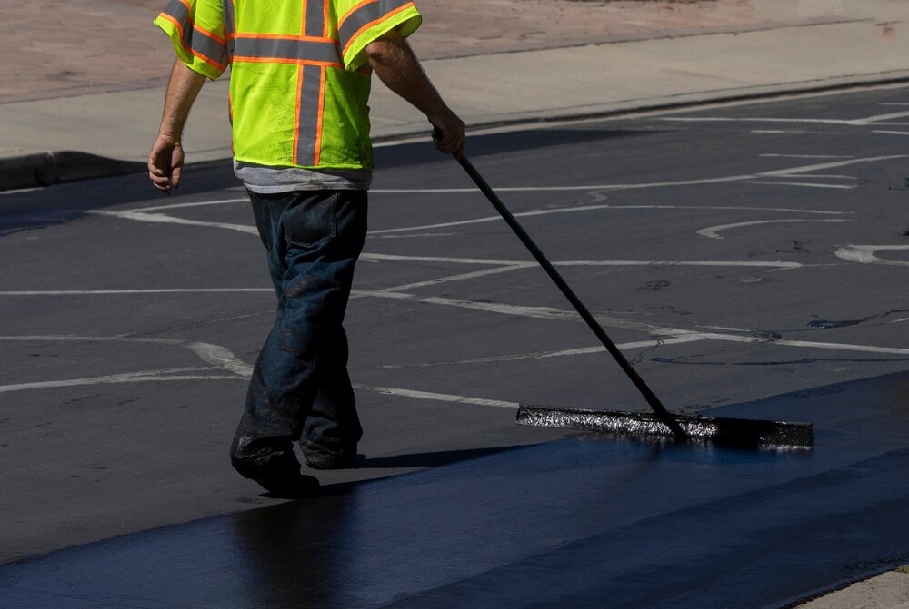 Paving Maintenance. Worker Using A Sealcoating Brush During Asphalt Resurfacing Project.